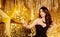Fashion Brunette Woman in Black Dress touching Big Golden Star over Gold Glitter Background. Happy Beauty Model Celebrating