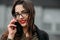 Fashion consept: beatiful young girl with long hair, glasses, red lips standing near modern wall wearing in green suit and grey je