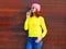 Fashion cool girl with coffee cup in colorful clothes over wooden background wearing pink hat yellow sweater