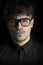 Fashion dark portrait of young man with glasses on black background. Portrait of intelligent man. Photo portrait curly guy