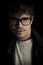 Fashion dark portrait of young man with glasses on black background. Portrait of intelligent man. Photo portrait curly man