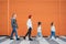 Fashion-dressed quartet of small kids and teenager sisters and brothers crossing a pedestrian zebra crosswalk on the orange wall