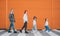 Fashion-dressed quartet of small kids and teenagers sisters and brothers crossing a pedestrian zebra crosswalk on the orange wall