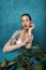 Fashion female tattooed model sitting at the table with cherry branch in front of blue background