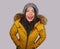 Fashion isolated portrait of young beautiful and happy Asian Korean woman in Winter hat and warm yellow feather jacket with fur