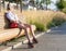 Fashion leggy girl in a beautiful high-heeled shoes in short denim shorts in the summer sitting on the bench in the headphones at