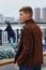 Fashion lifestyle. A young man in a brown leather jacket and jeans on the city embankment. The country is China across