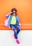 Fashion little girl child wearing a sunglasses, shirt, jeans and backpack over colorful orange