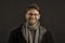 Fashion model with beard smile on dark background. Happy man in glasses on bearded face. Bearded man in scarf and coat