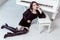 Fashion model with black dress and boots with smokey eyes makeup and hairstyle sitting on floor and posing near with piano