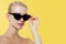 Fashion Model girl isolated over yellow background. Beauty stylish blonde woman posing in retro black sunglasses. Casual