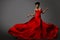 Fashion Model in Red Long waving Luxury Dress. Dark Skinned Beauty Woman with Afro Black Hairstyle dancing over Gray Background.