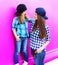 Fashion mother looking at child little girl in checkered shirts and baseball caps in city on colorful pink wall