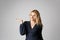 Fashion photo of a beautiful blonde woman in a pretty dress posing with hand over gray empty background. Fashionable