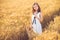 Fashion photo of a little girl in white dress and straw hat at the evening wheat field