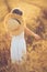 Fashion photo of a little girl in white dress and straw hat at the evening wheat field