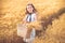 Fashion photo of a little girl in white dress and straw hat at the evening wheat field