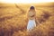 Fashion photo of a little girl in white dress and straw hat at the evening wheat field