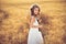 Fashion photo of a little girl in white dress and straw hat at the evening wheat field