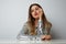 Fashion portrait of a beautiful smiling woman in a pretty silver dress with tinsel sitting at the table over empty light