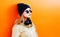 Fashion portrait blonde woman with headphones, sunglasses and black hat on a orange colorful background