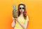 Fashion portrait cool girl in sunglasses with pineapple over colorful orange