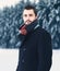 Fashion portrait handsome elegant bearded man wearing black coat in winter over snowy trees forest background