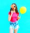 Fashion portrait pretty young woman wearing pink t-shirt, denim shorts with yellow air balloon, lollipop candy over colorful blue