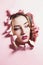 Fashion portrait of a young woman tearing a hole in pink cardboard paper, face of a girl with makeup, creative concept freedom in