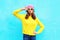 Fashion pretty cool girl in headphones listening to music wearing a colorful pink hat yellow sunglasses and sweater over blue