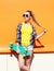 Fashion pretty girl wearing a sunglasses with skateboard over colorful orange