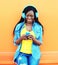 Fashion pretty smiling african woman with headphones listens to music over orange