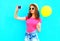 Fashion pretty smiling young woman taking picture self portrait on smartphone with yellow air balloon wearing a pink t-shirt