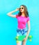 Fashion pretty woman holds skateboard over colorful blue