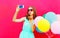 Fashion pretty woman taking a picture on a smartphone sends an air kiss over an air colorful balloons pink background
