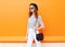 Fashion pretty woman wearing a black hat sunglasses white pants and handbag clutch over colorful orange