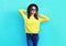 Fashion pretty woman wearing black hat and yellow knitted sweater over colorful blue