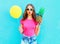 Fashion pretty woman with yellow air balloon and pineapple wearing a pink t-shirt over colorful blue