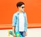 Fashion profile teenager boy with skateboard poses on colorful
