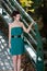 Fashion slim woman wearing green dress standing against bridge