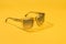 Fashion sunglasses in sunlight on summer pastel yellow background. Woman stylish eyeglasses for banner. Transparent