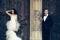 Fashion wedding couple of bride in white bride dress and handsome man in black groom suit near wooden door with iron