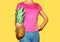 Fashion woman holds in hands pineapple over colorful yellow background