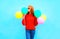 Fashion woman kisses an air colorful balloons on a blue