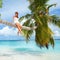 Fashion woman siting upon palm tree on the beach