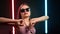 Fashion woman in sunglasses dancing raising hands at illuminated glow flashing dance floor nightclub