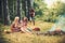 Fashion women in retro dresses relax at bonfire. Happy women with blurred man in summer forest. Beauty girls with long