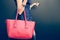 Fashionable beautiful big red handbag on the arm of the girl in a fashionable black dress, posing near the wall on a warm summer n