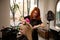 Fashionable beautiful red-haired female hairdresser using a round comb and hair dryer straightens blonde hair to a client of a