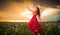 Fashionable beautiful young woman in long red dress posing outdoor with cloudy dramatic sky in background. Attractive brunette